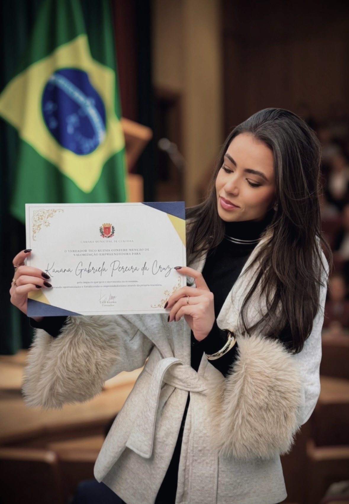 A arquiteta Kauana Cruz, da KRUZ Arquitetura, exibe o certificado de reconhecimento institucional e destaque profissional recebido da Câmara Municipal de Curitiba.